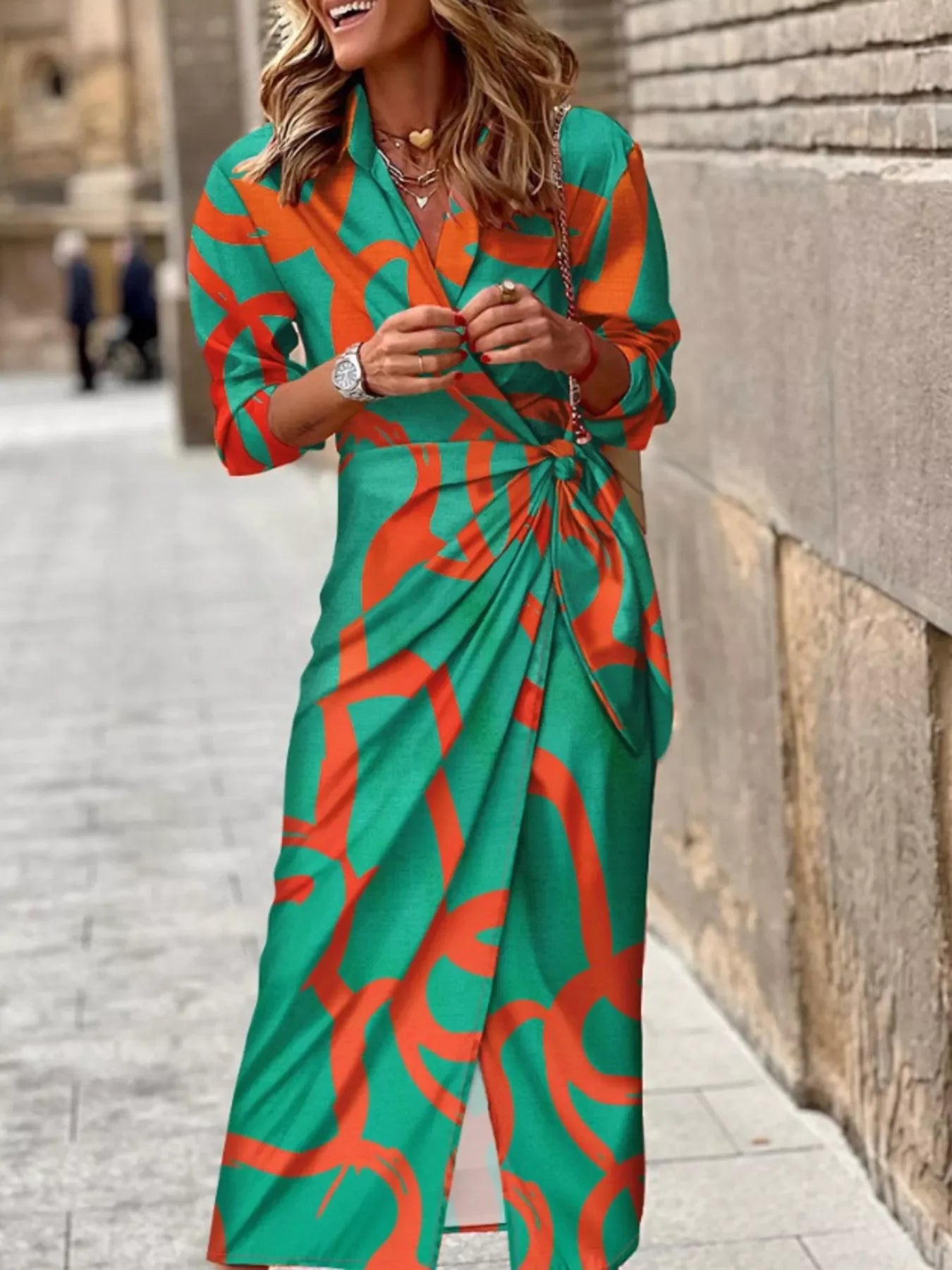 Woman wearing long green and orange abstract print wrap dress with 3/4 sleeves walking on city sidewalk
