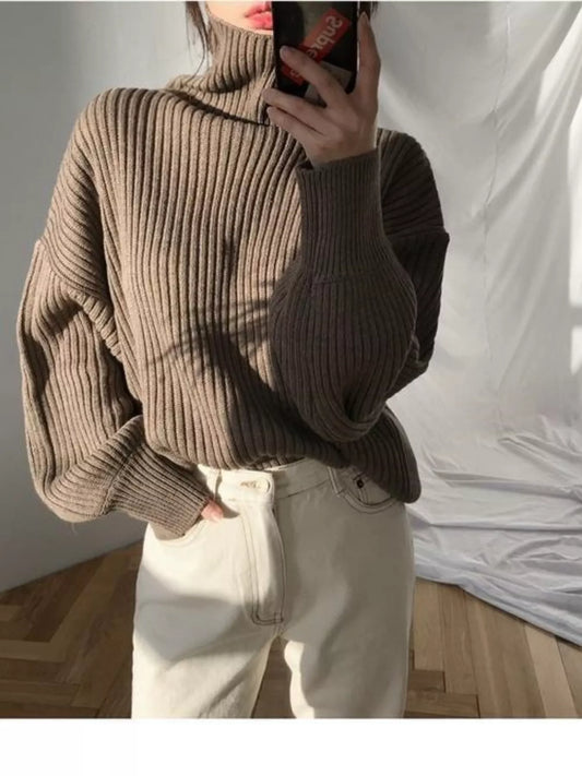 Woman wearing a brown ribbed turtleneck oversized sweater and white trousers.
