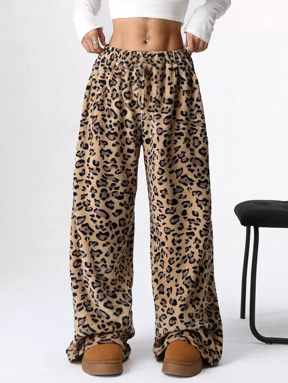 Woman wearing leopard print fleece lounge pants with a white cropped long sleeve top and brown slippers