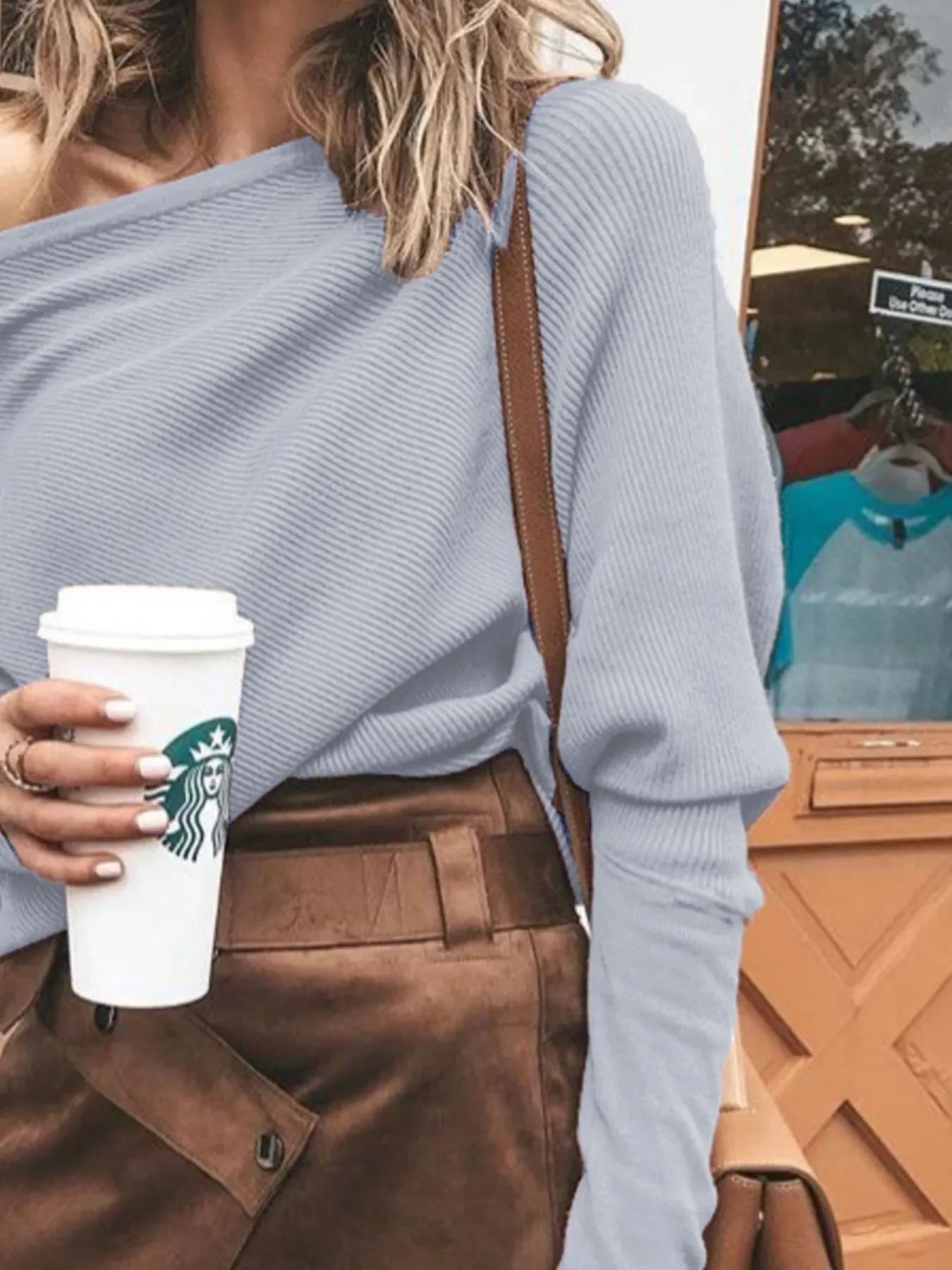Woman in light gray ribbed sweater and brown leather skirt holding Starbucks coffee cup outdoors