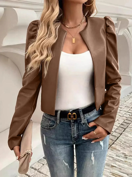 Woman wearing a brown faux leather puff sleeve jacket, white top, and distressed blue jeans.