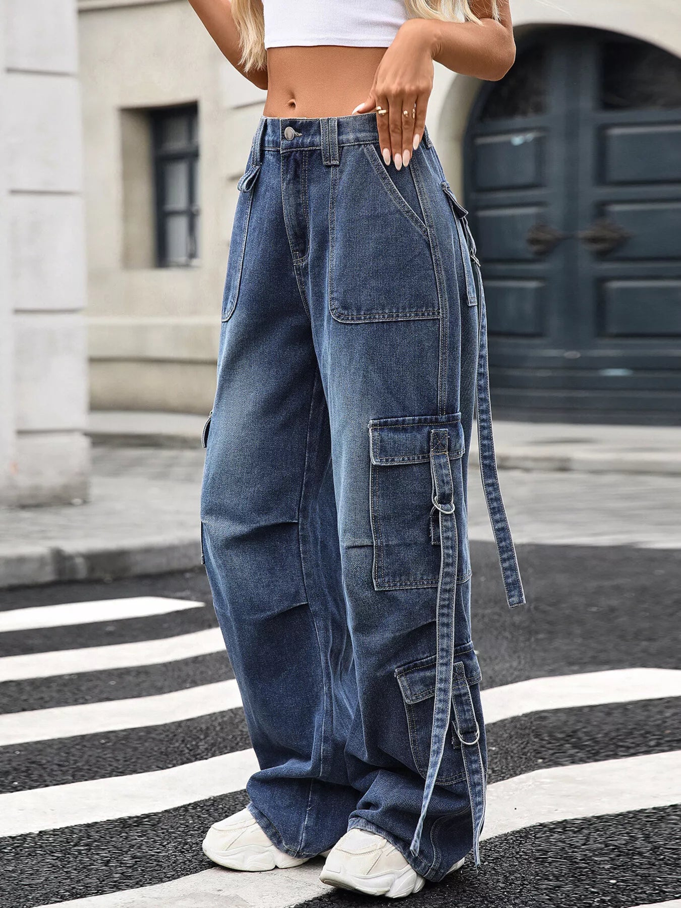 Wide-leg denim cargo pants with side straps and pockets, paired with white sneakers for street style