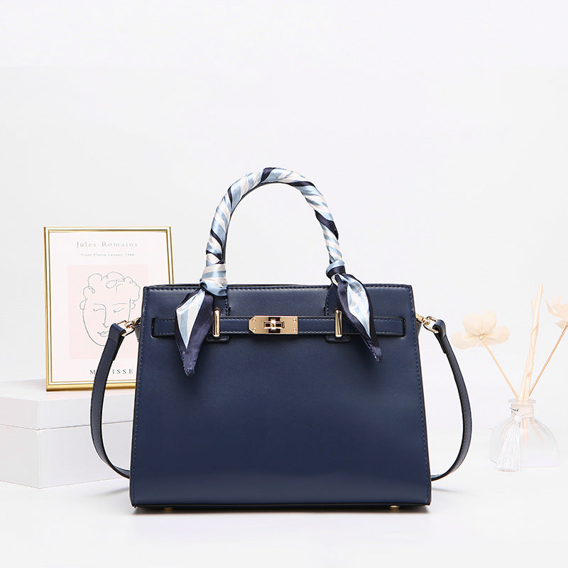 Navy blue structured handbag with gold hardware and silk scarf handles on white table