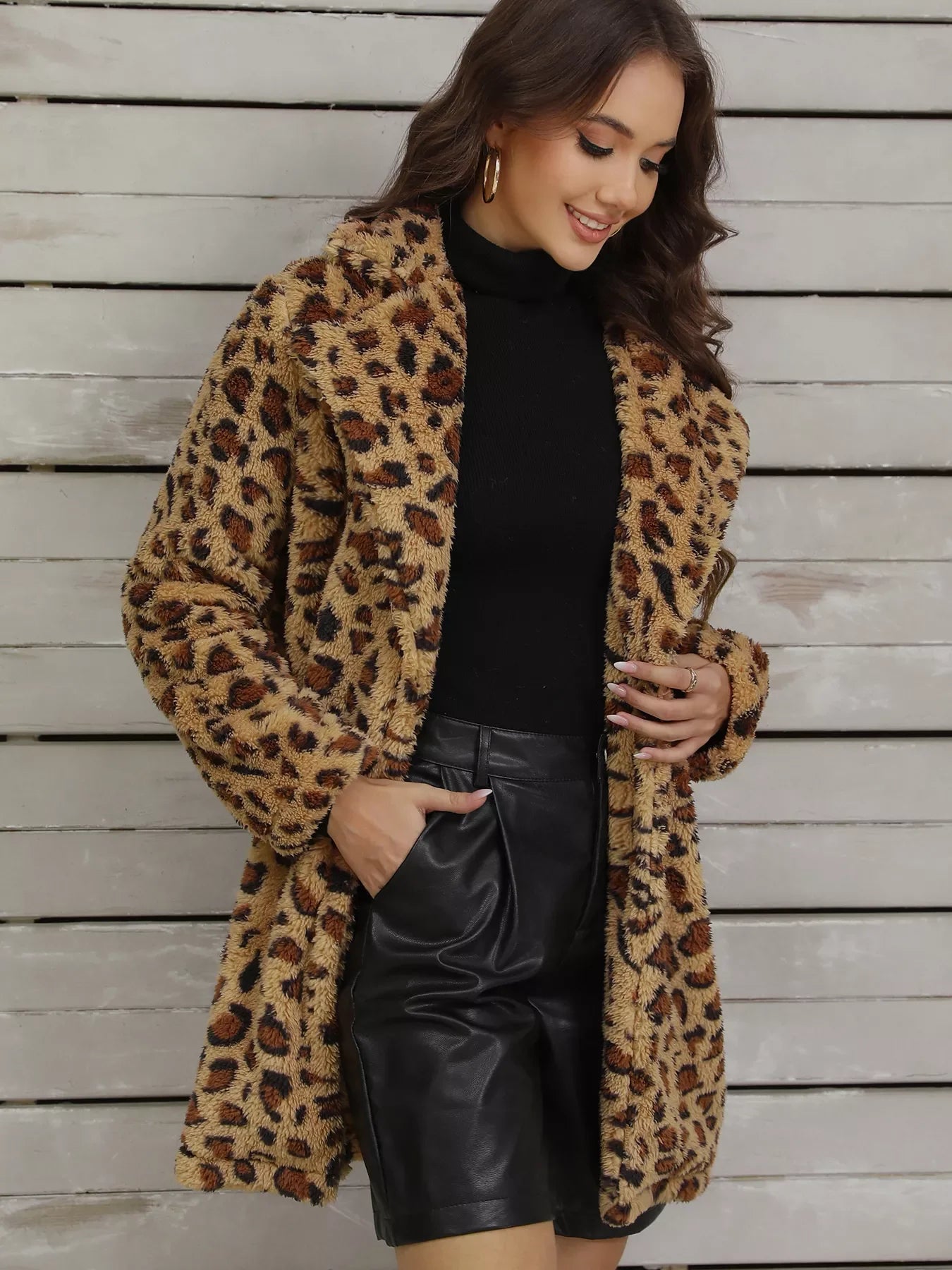 Woman wearing leopard print faux fur coat, black turtleneck, and black leather shorts against wooden wall