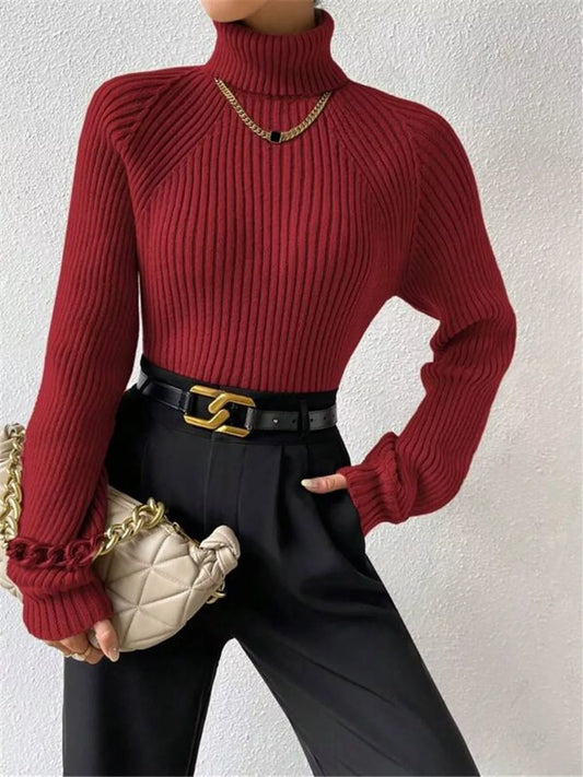 Woman wearing a red ribbed turtleneck sweater, black trousers, and a gold chain necklace.