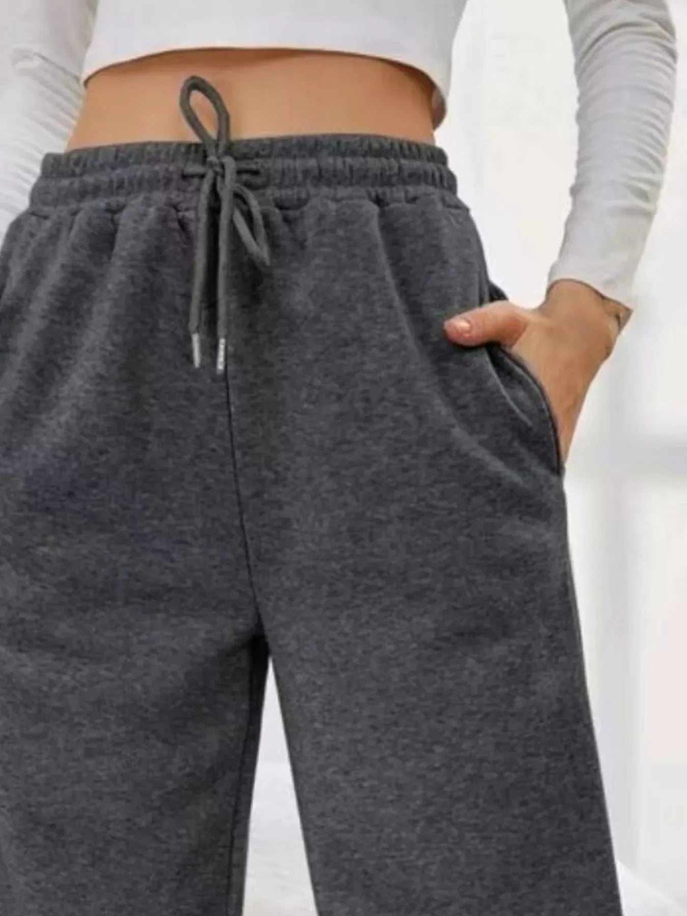 Close-up of woman wearing dark gray drawstring sweatpants with hand in pocket and white crop top