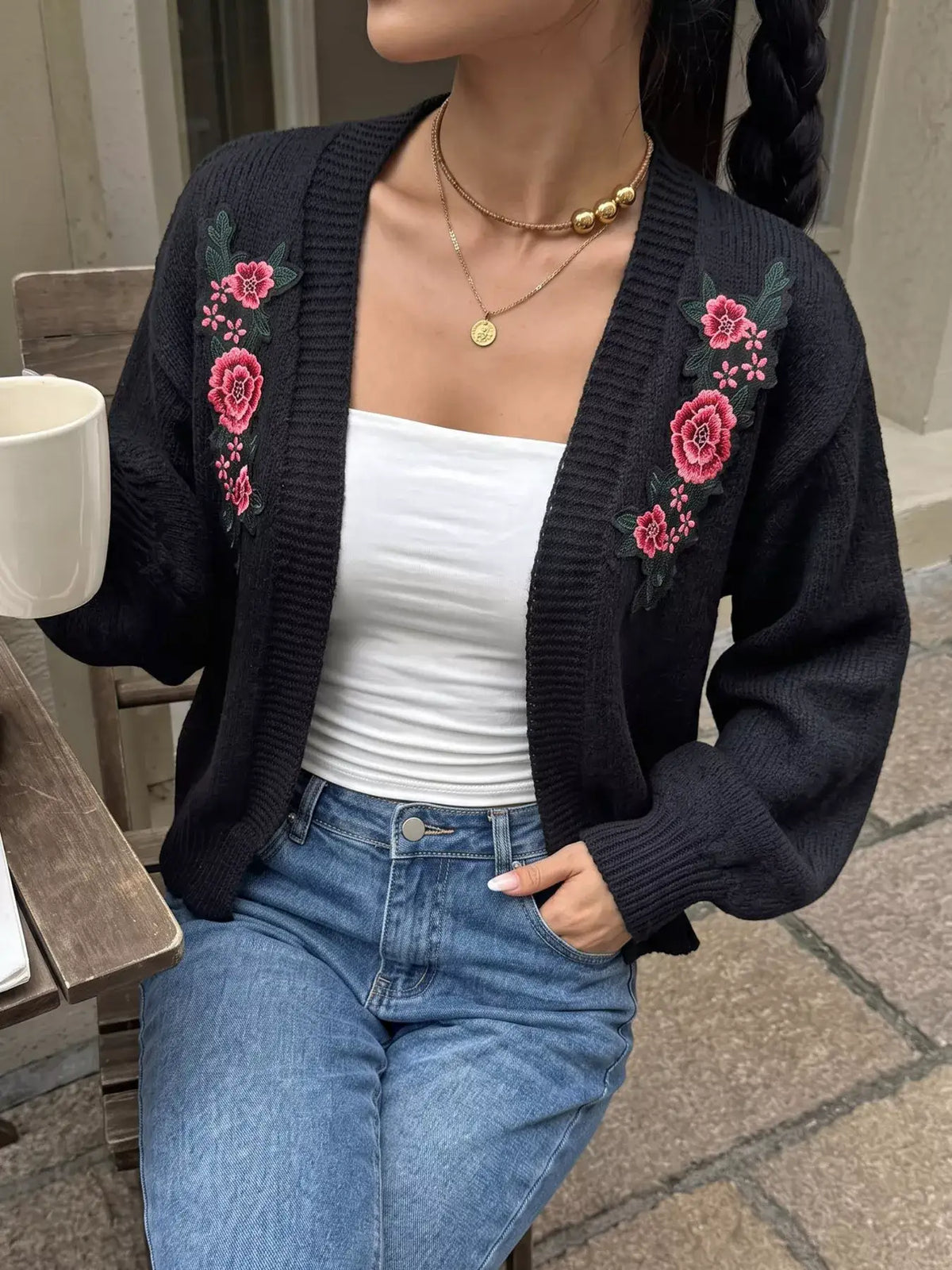 Evie's Dreamland black knit cardigan with pink floral embroidery, worn over a white top and blue jeans.