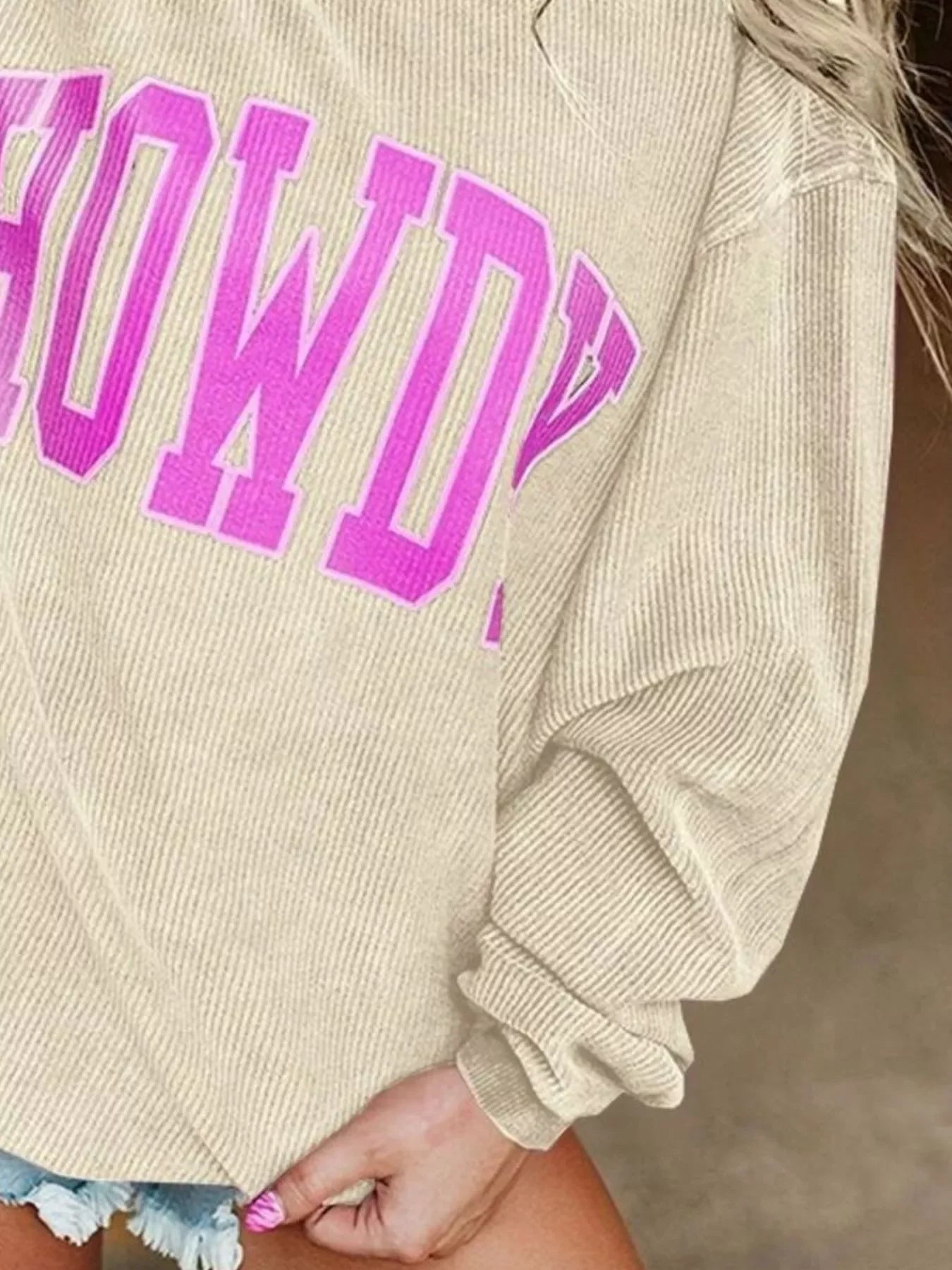 Beige ribbed sweater with large pink 'COWBOY' text detail worn with denim shorts