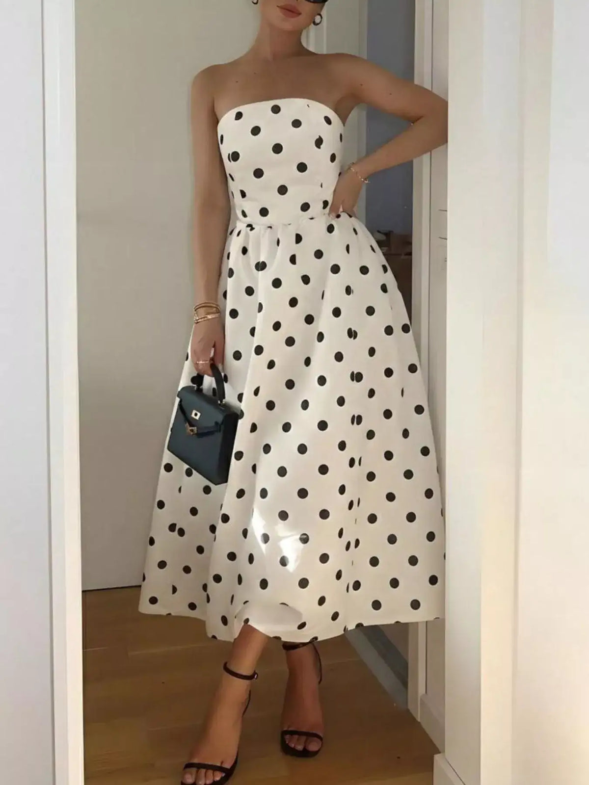 Evie's Dreamland white strapless midi dress with black polka dots, paired with a black handbag.