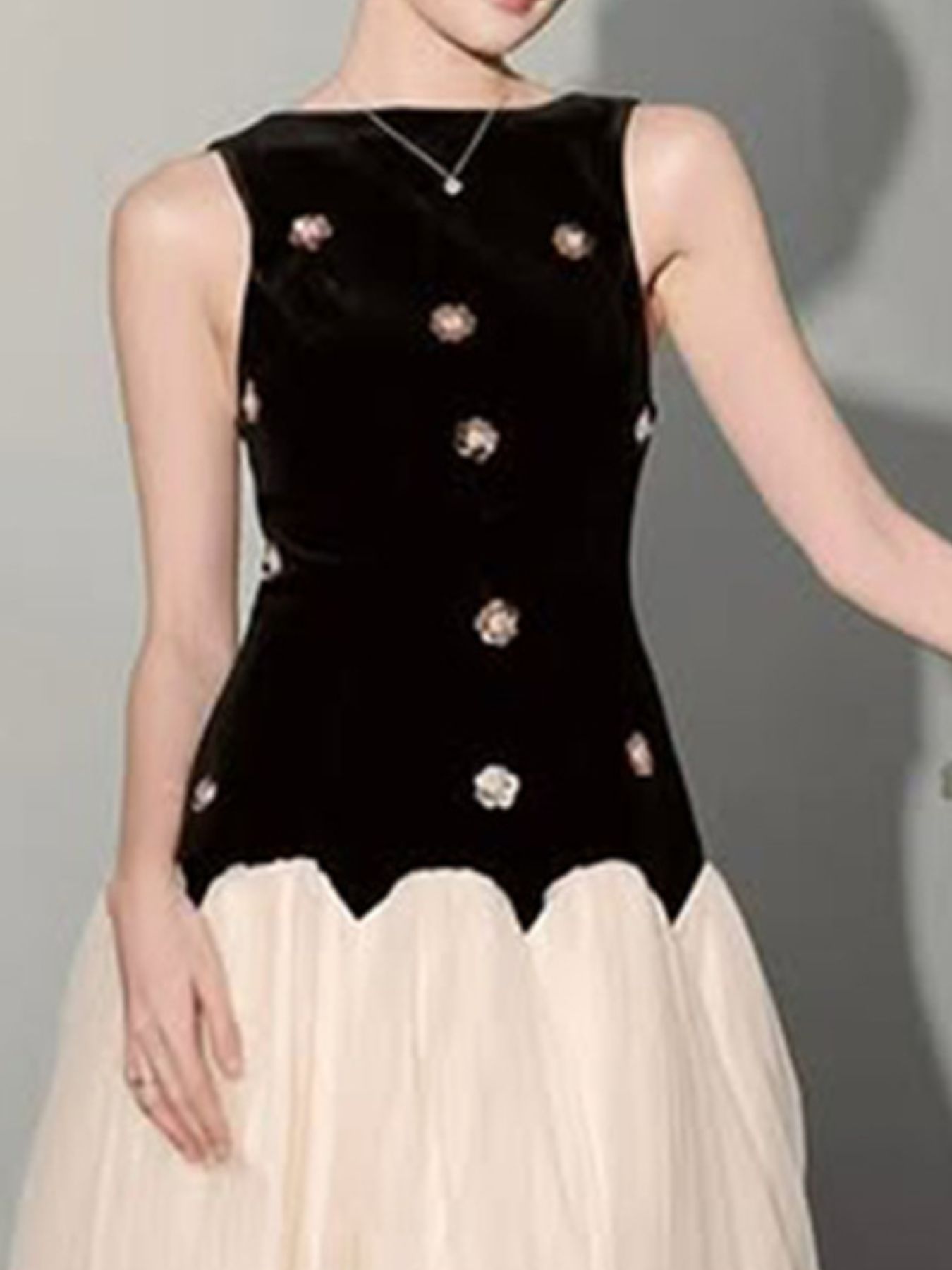 Woman wearing a sleeveless black velvet bodice with floral embellishments and a cream tulle skirt.