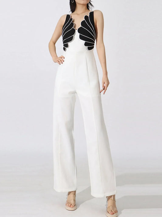 Woman wearing white wide-leg jumpsuit with black leaf-like pattern on bodice and beige sandals