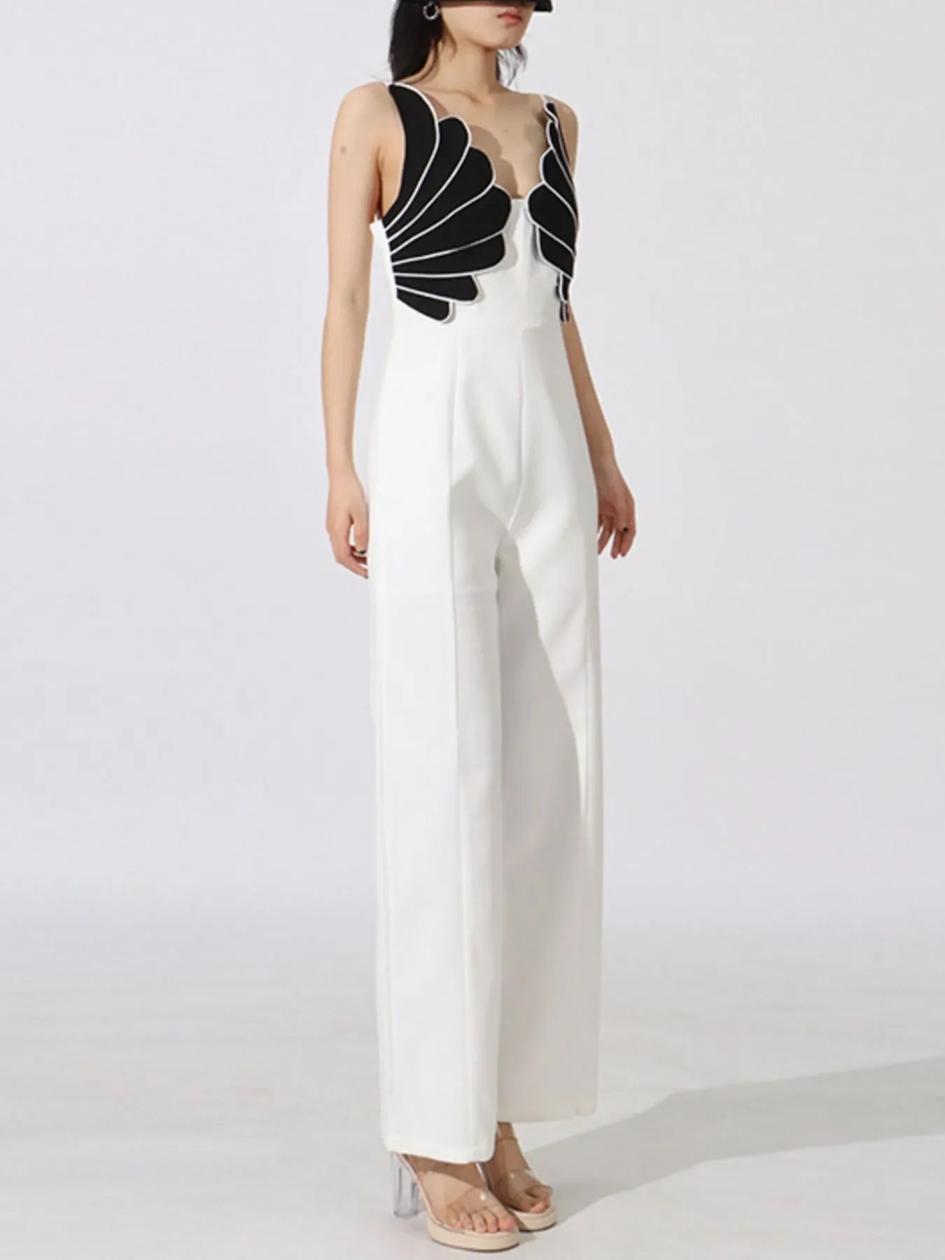 Woman wearing white wide-leg jumpsuit with black scallop detail on top and clear high heels