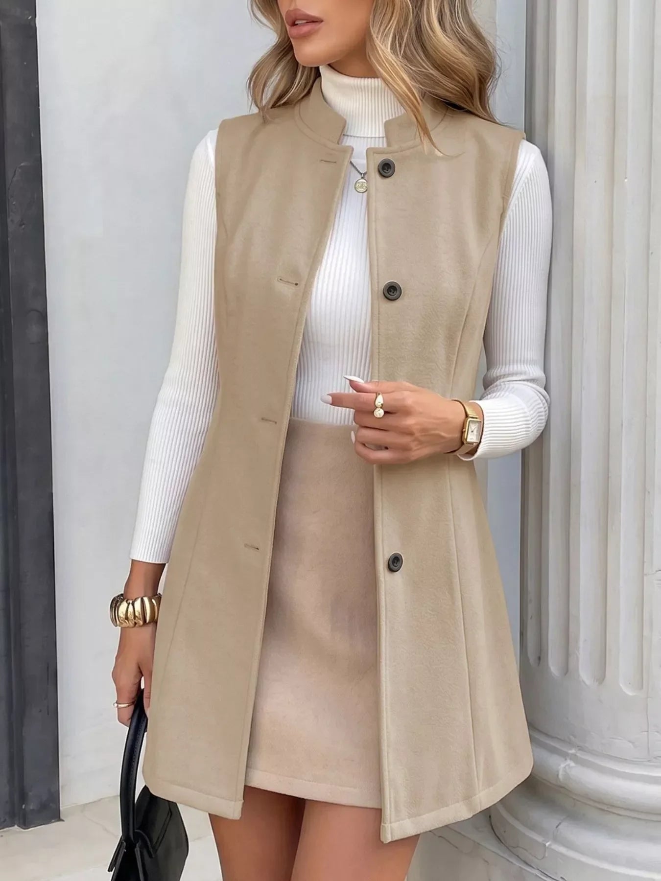 Woman wearing a beige button-up sleeveless vest over a white ribbed turtleneck and matching skirt.