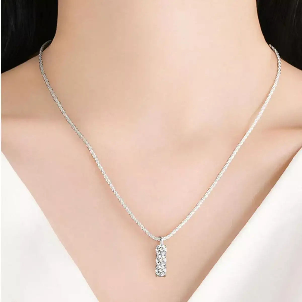 Moissanite 925 sterling silver bar necklace with three round crystals on a thin chain worn by a woman.