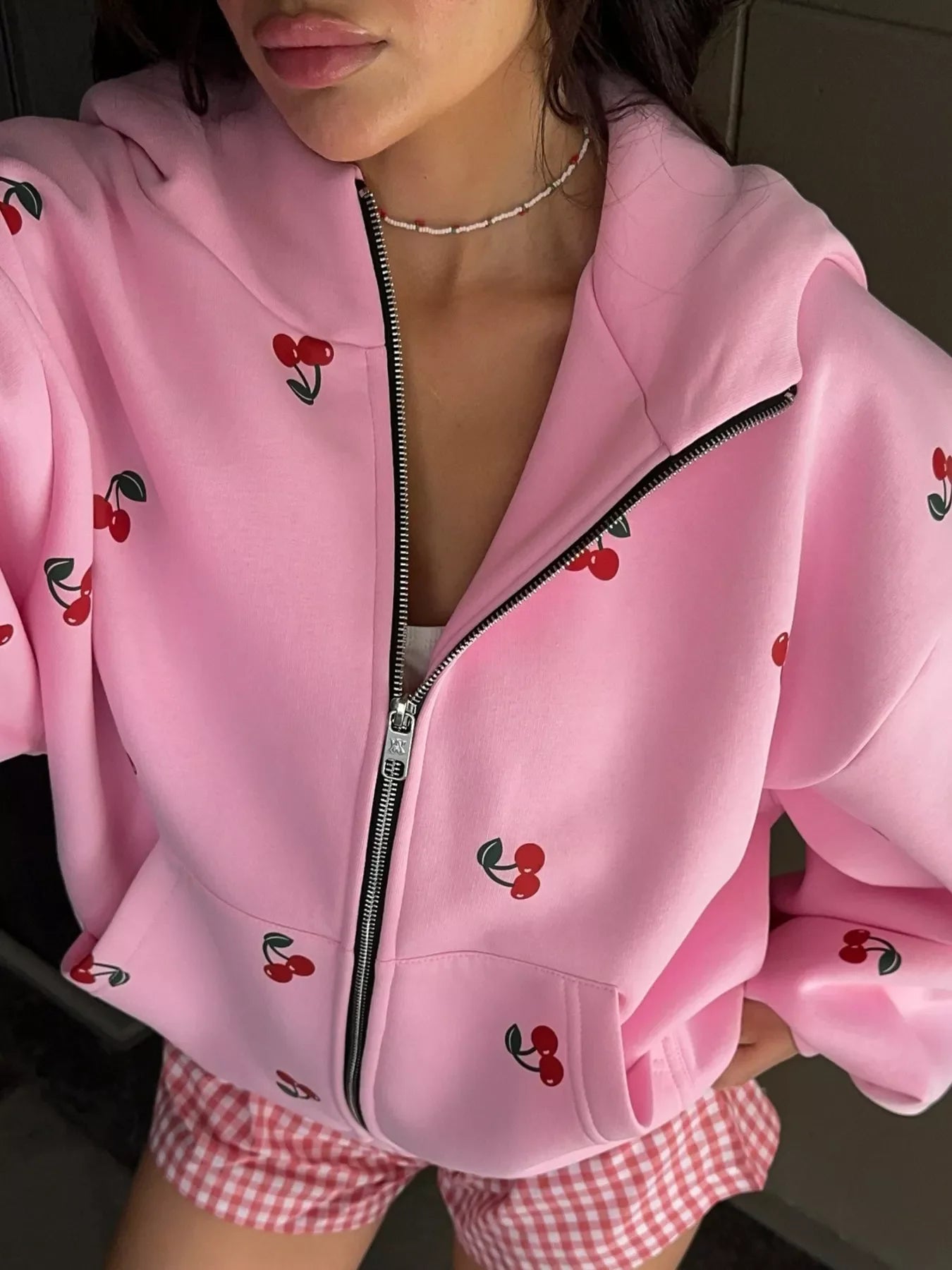 Close-up of woman wearing pink zip-up hoodie with cherry print and pink checkered shorts