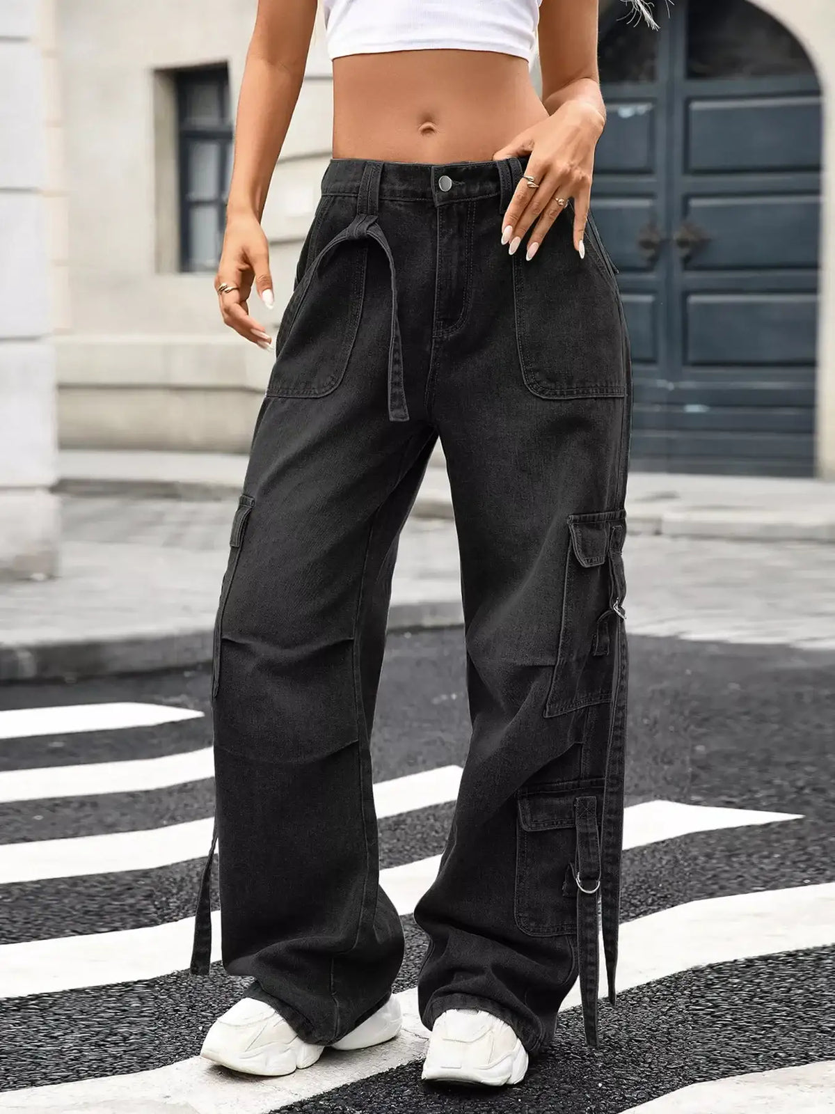 Black cargo pants with side pockets and drawstring waist, styled with white sneakers on urban street
